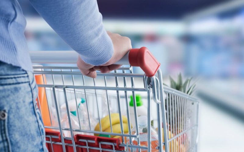 Woman doing grocery shopping at the supermarket, she is pushing a shopping cart, hand close up